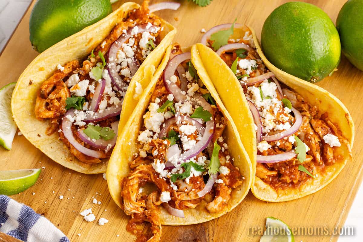 chicken tinga tacos on a wooden cutting board next to limes
