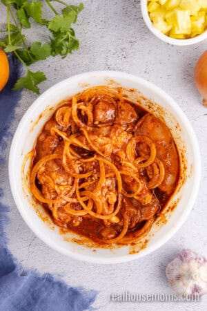 chicken thighs and sliced onion mixed with al pastor marinade in a bowl