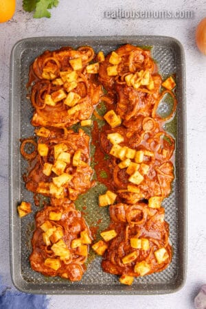 marinated chicken al pastor topped with pineapple chunks on a baking sheet