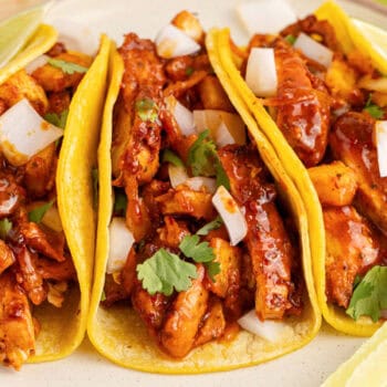 square image of three chicken al pastor tacos on a plate