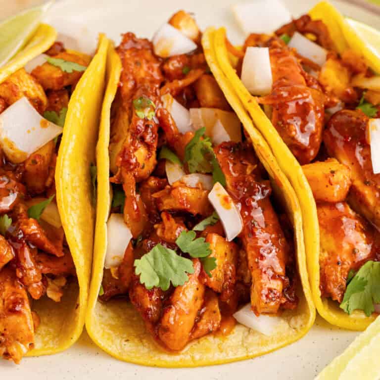 square image of three chicken al pastor tacos on a plate