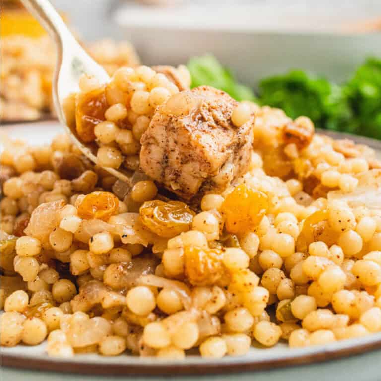 square image of a bite of chicken and israeli couscous on a fork over the plate
