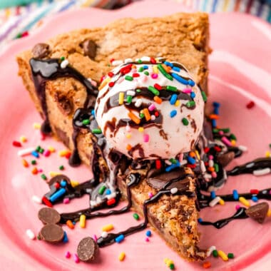 square close up image of a slice of chocolate chip skillet cookie with ice cream, sprinkles, and chocolate sauce on top