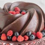 square image of chocolate coated chocolate pound cake with berries on a cake stand