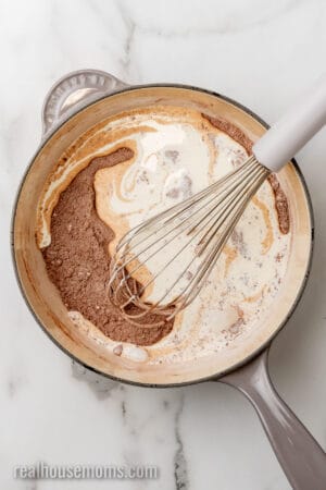 heavy cream being whipped into cocoa powder, sugar, cornstarch, and salt in a saucepan