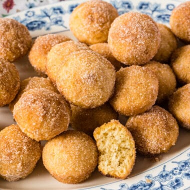 square image of churro muffins piled on a plate with a bite taken out of one