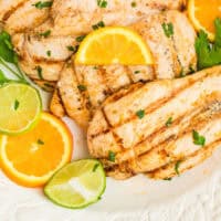 grilled citrus chicken breasts on a platter with orange and limes slices with recipe name at the bottom