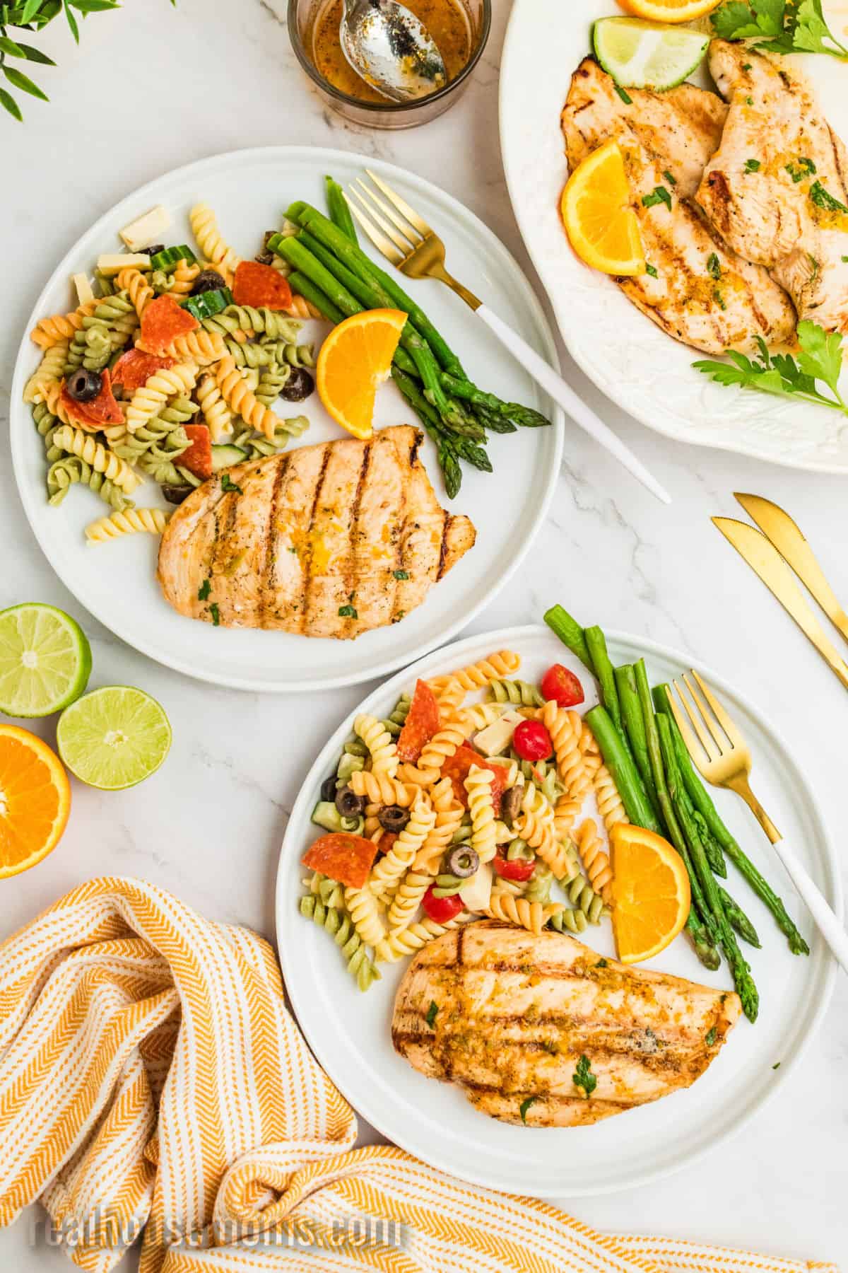 grilled citrus chicken on plate with pasta salad and asparagus next to the platter of chicken