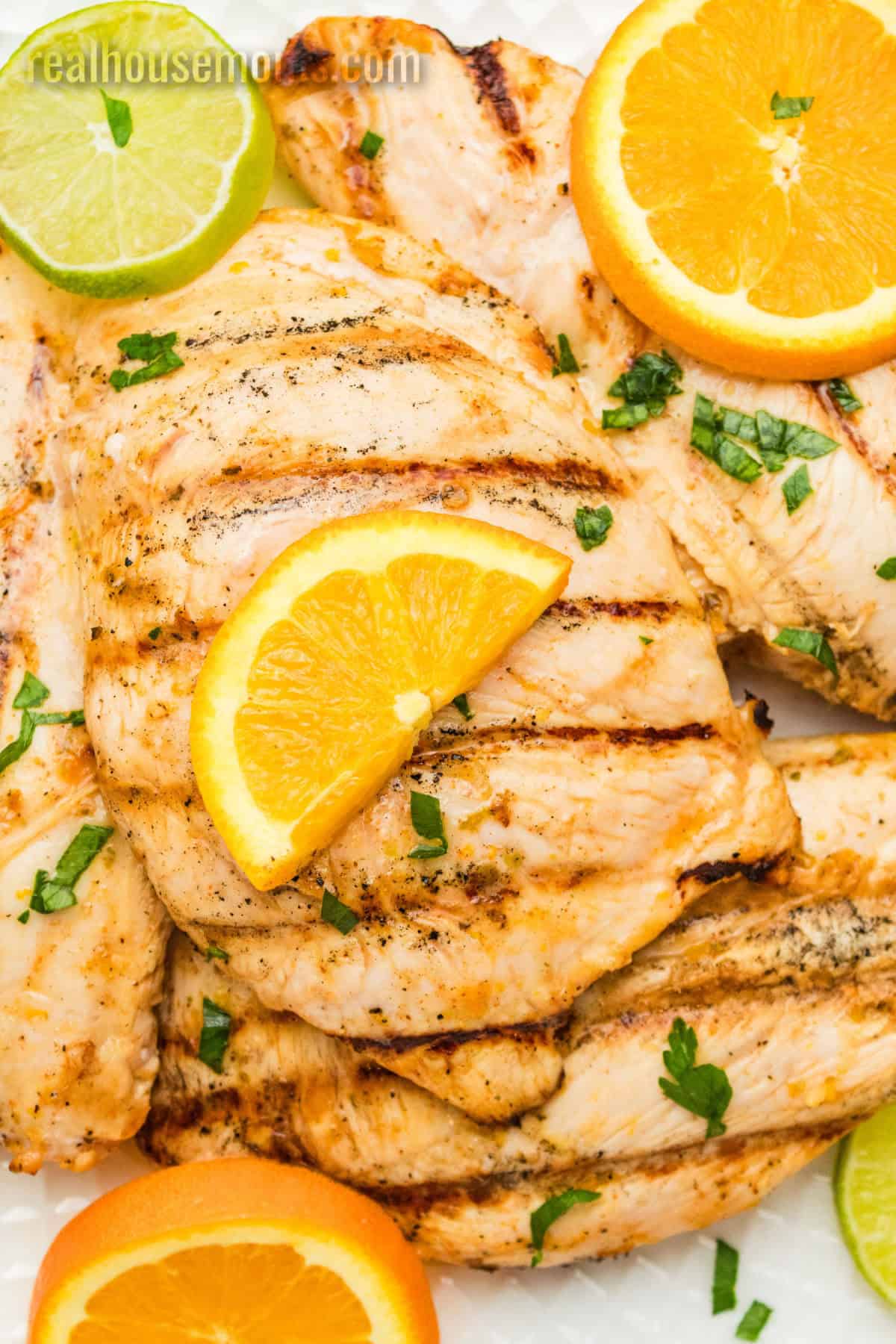 close up of grilled citrus marinated chicken on a platter with orange and lime slices for garnish