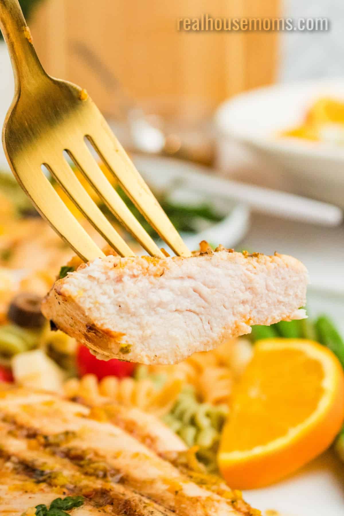 bite of citrus marinated chicken on a fork over the plate
