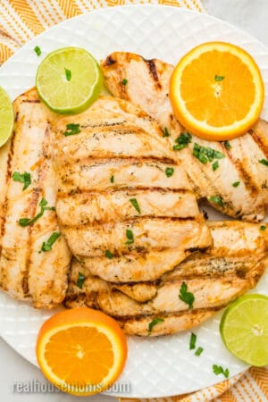 grilled citrus chicken on a platter with chopped parsley and citrus slices for garnish