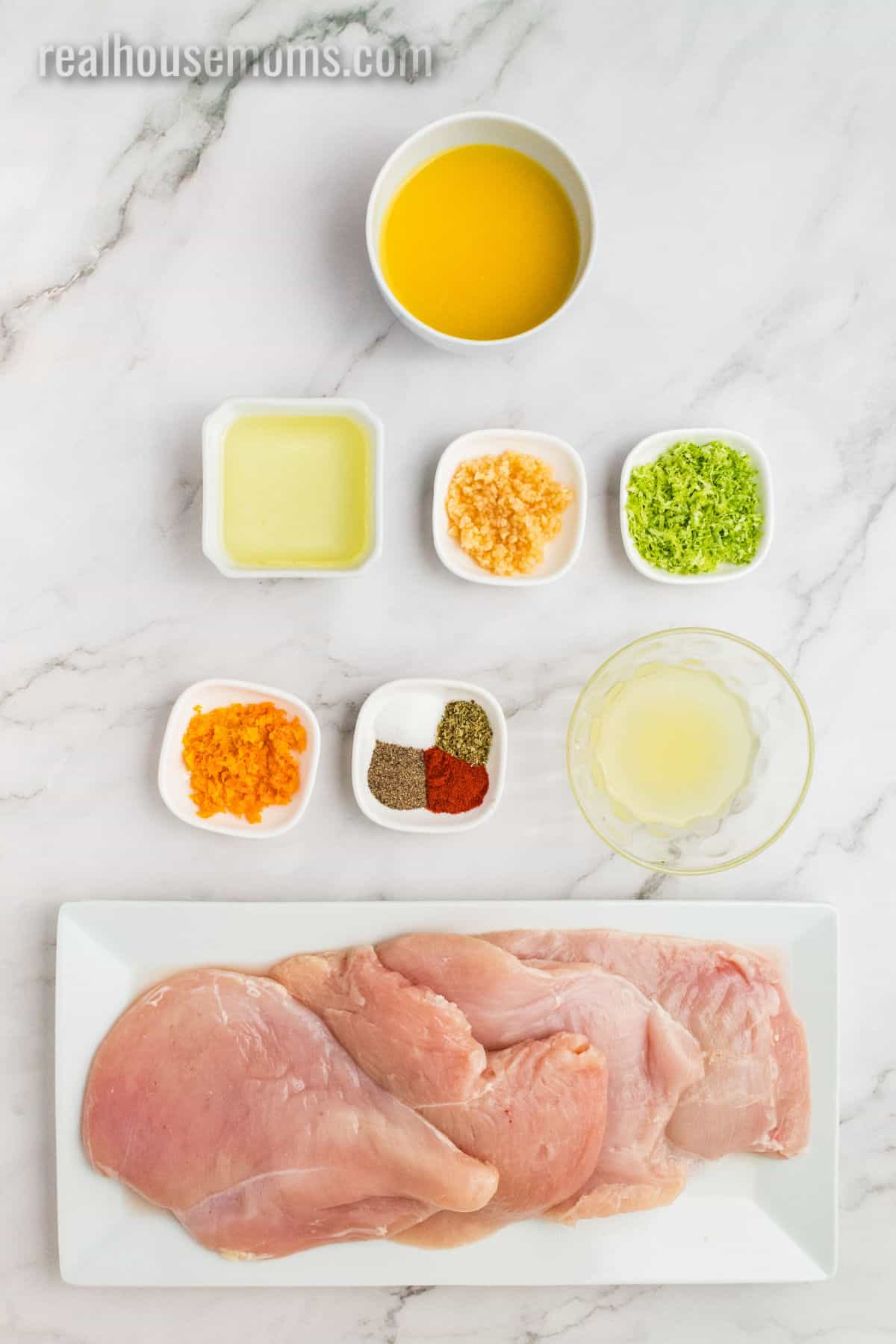 ingredients to make citrus chicken marinade laid out on a counter next to raw chicken breasts