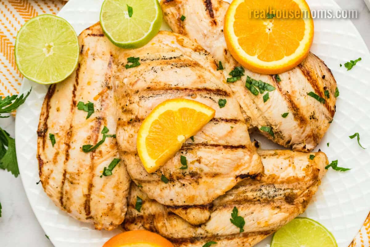 grilled citrus marinated chicken breasts with chopped parsley, orange, and lime slices on a platter
