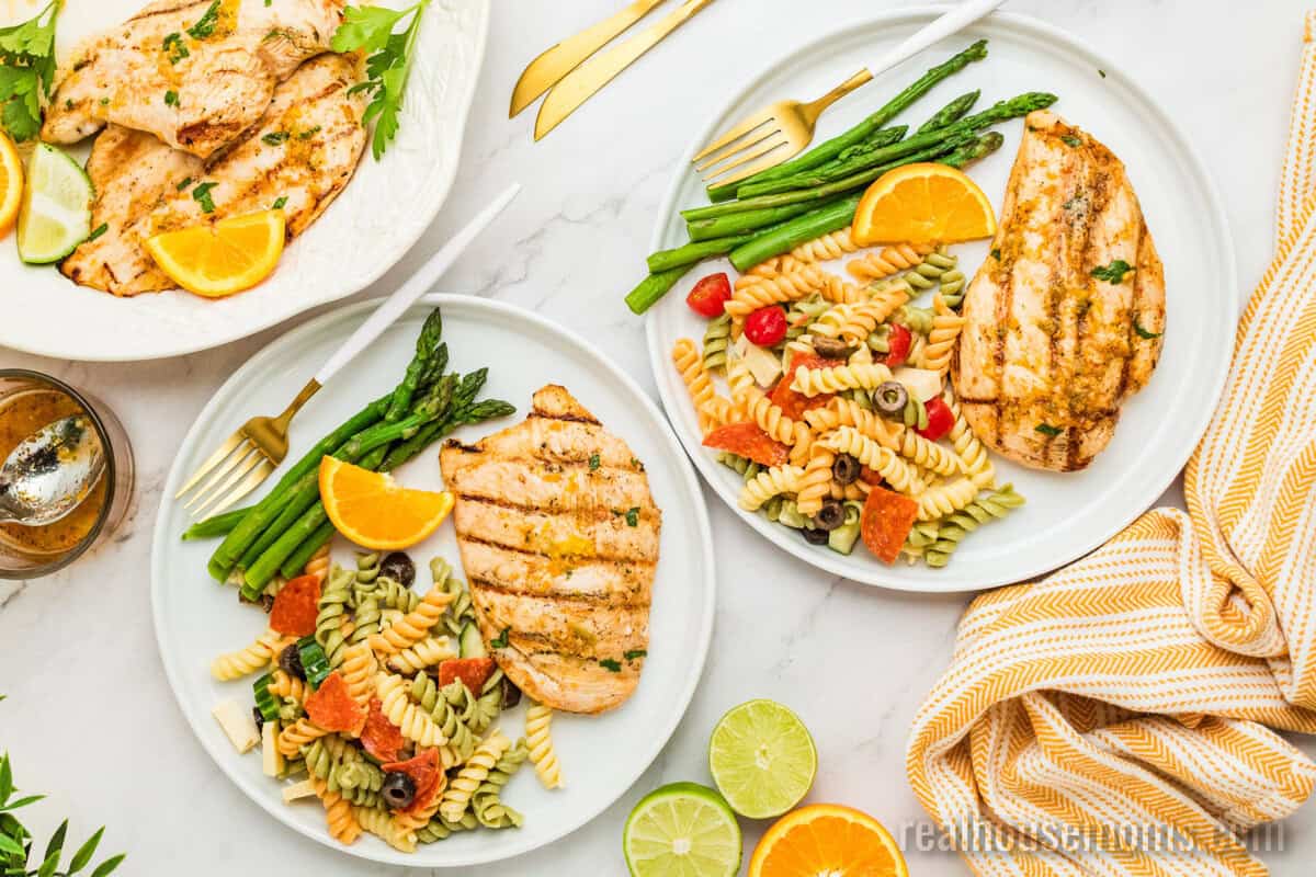 citrus marinated grilled chicken on plates with asparagus, pasta salad, and forks