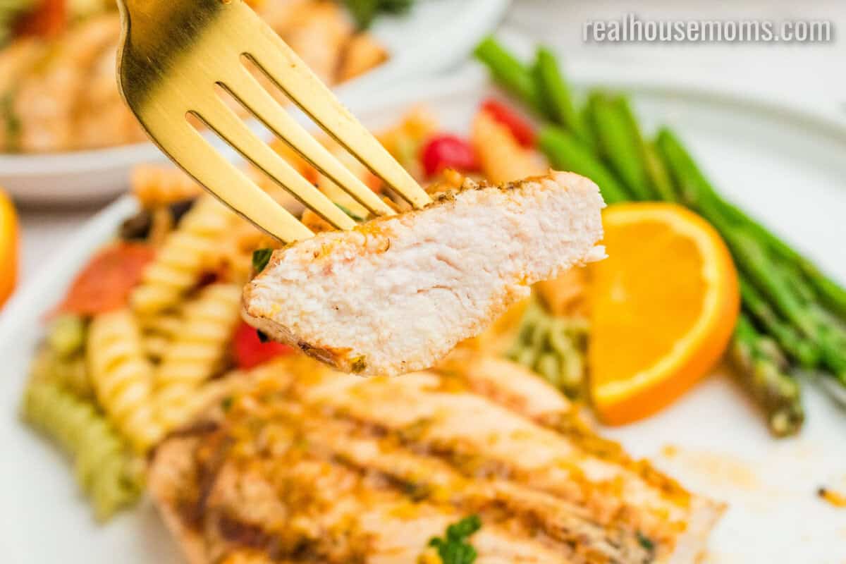 bite of grilled citrus chicken on a fork over the plate