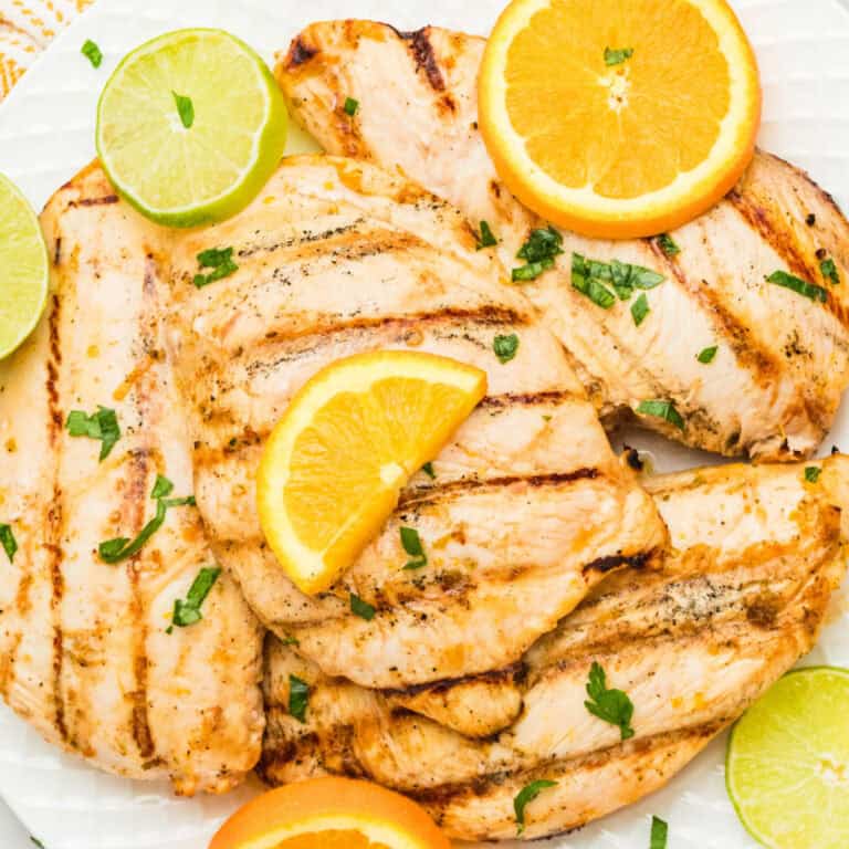 square image of grilled citrus marinated chicken on a white plate with orange and lime slices