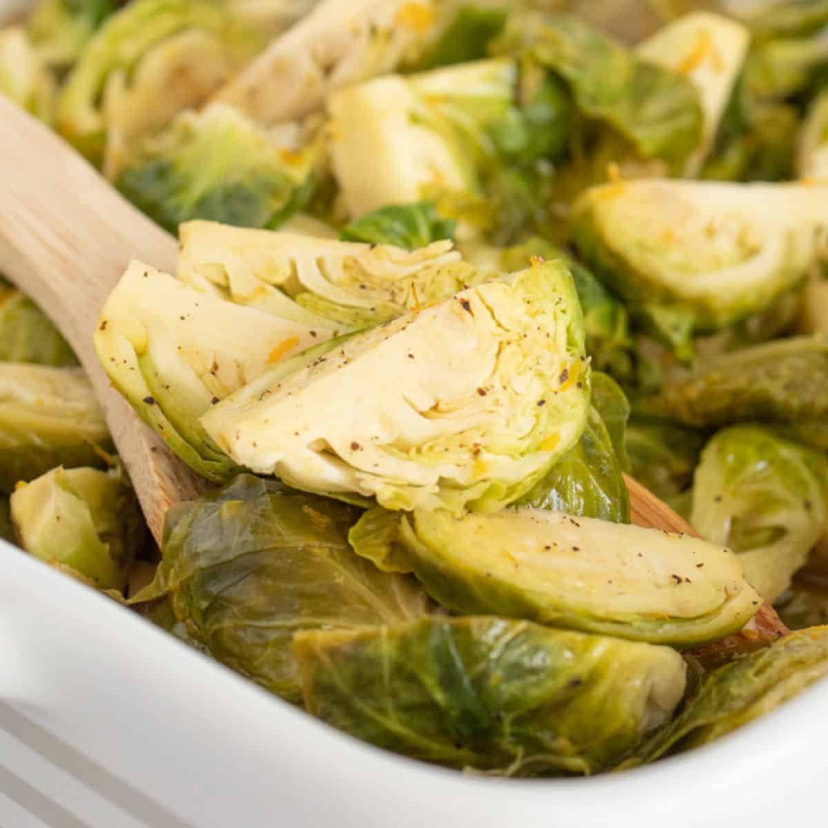 square image of roasted brussels sprouts in a baking dish with a wooden spoon