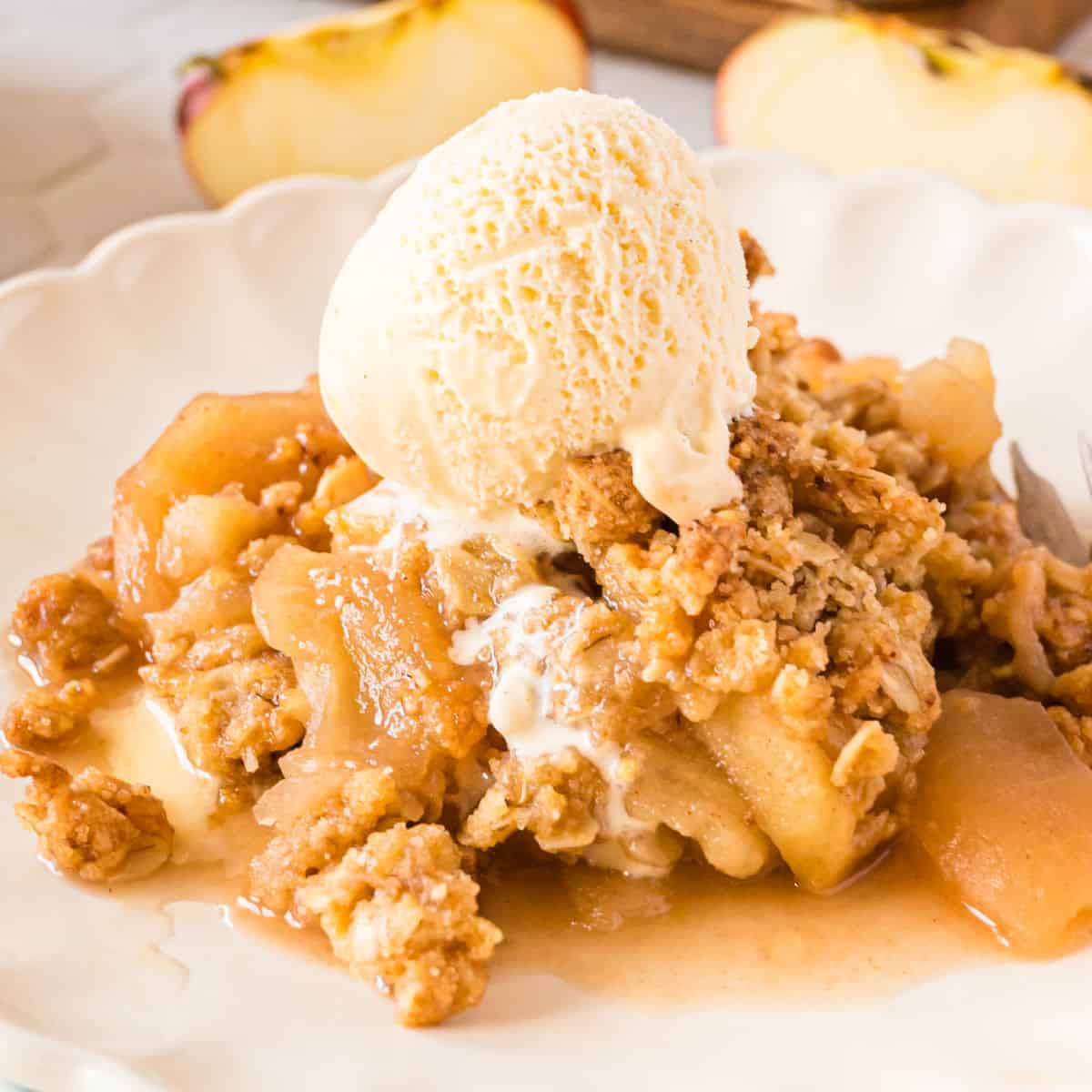 square image of classic apple crisp on a plate with vanilla ice cream