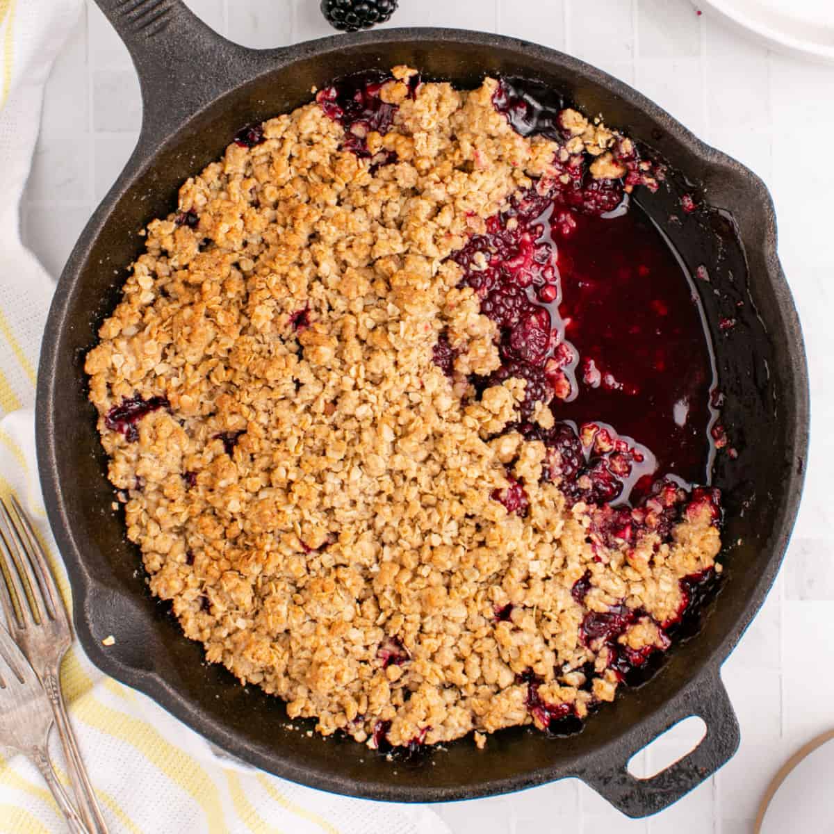 square image of blackberry crumble in a skillet with a portion taken out showing the berries and sauce under the topping