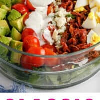 cobb salad in a glass bowl with ranch dressing being spooned over top with recipe name at bottom