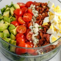 square image of cobb salad in a glass bowl with toppings arranged in lines