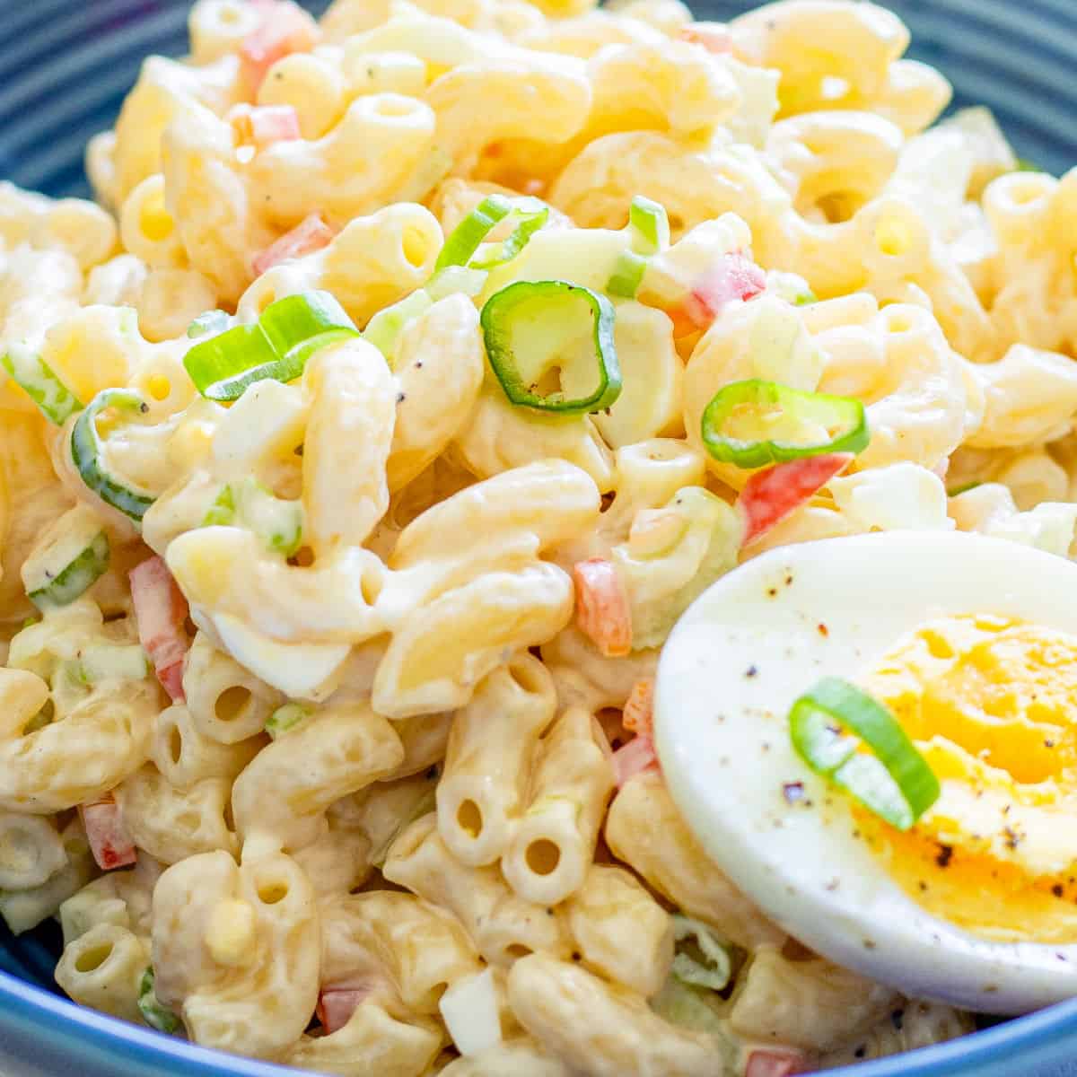 close up of macaroni salad in a blue bowl with half of a hard boiled egg