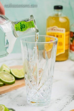 silver tequila being poured into a glass cocktail shaker