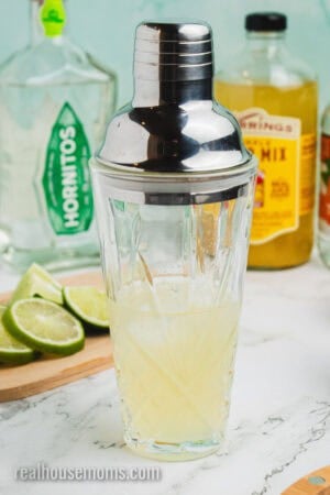 glass cocktail shaker with the silver lid on after margarita ingredients and ice have been added