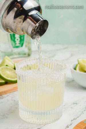 margarita recipe being strained into a salt rimmed rocks glass with ice