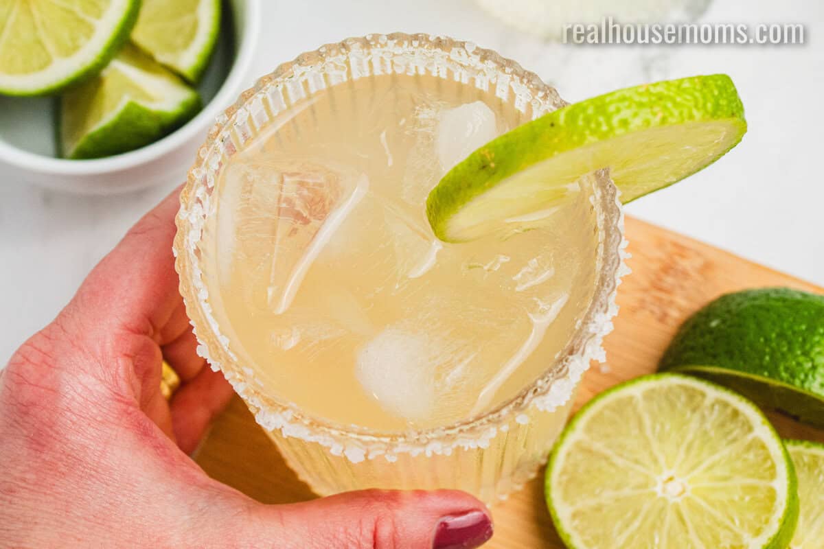 looking down at a hand grabbing a margarita from a wooden tray