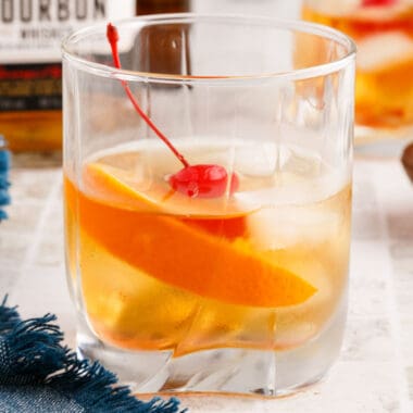square image of an old fashioned cocktail in front of a bottle of bourbon