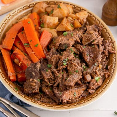 square image of classic pot roast on a serving platter with chopped parsley, carrots, and potatoes
