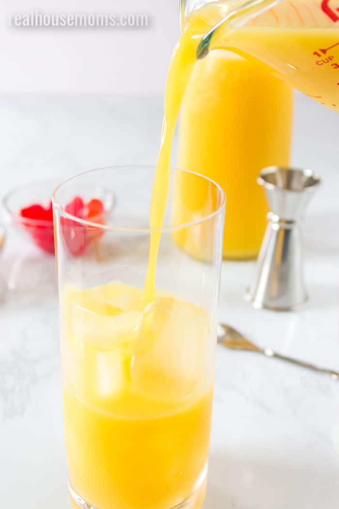 orange juice, grand marnier, and tequila being poured into a glass over ice