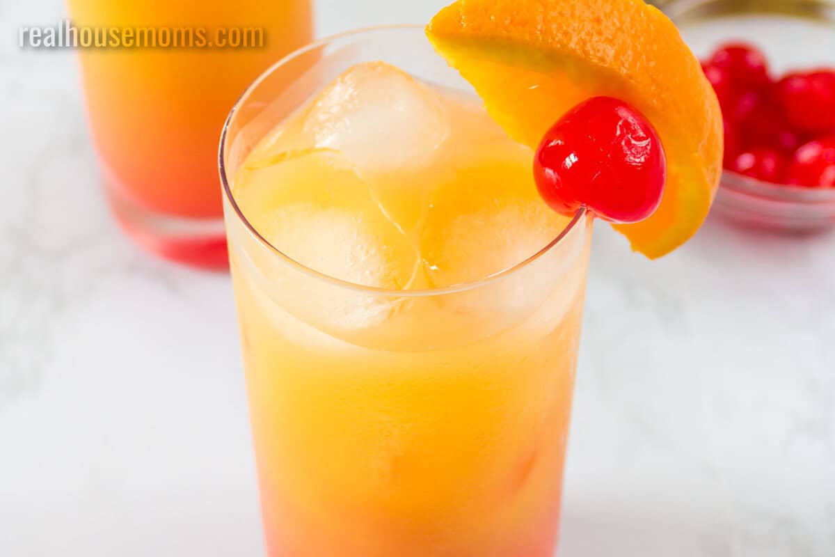 close up of a tequila sunrise with and orange slice and cherry garnish