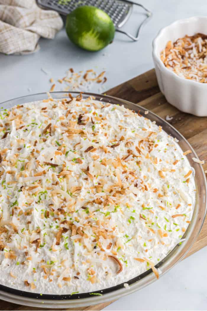 coconut cream pie in a pie plate with toasted coconut and lime zest on top