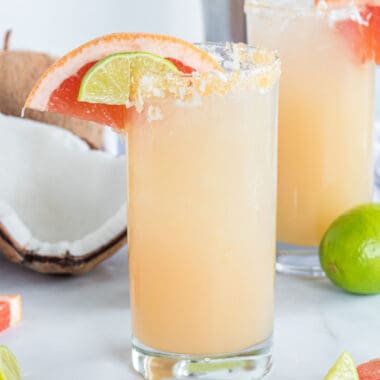 square image of a coconut tequila and grapefruit cocktail with fruit garnish and sugar & coconut rim