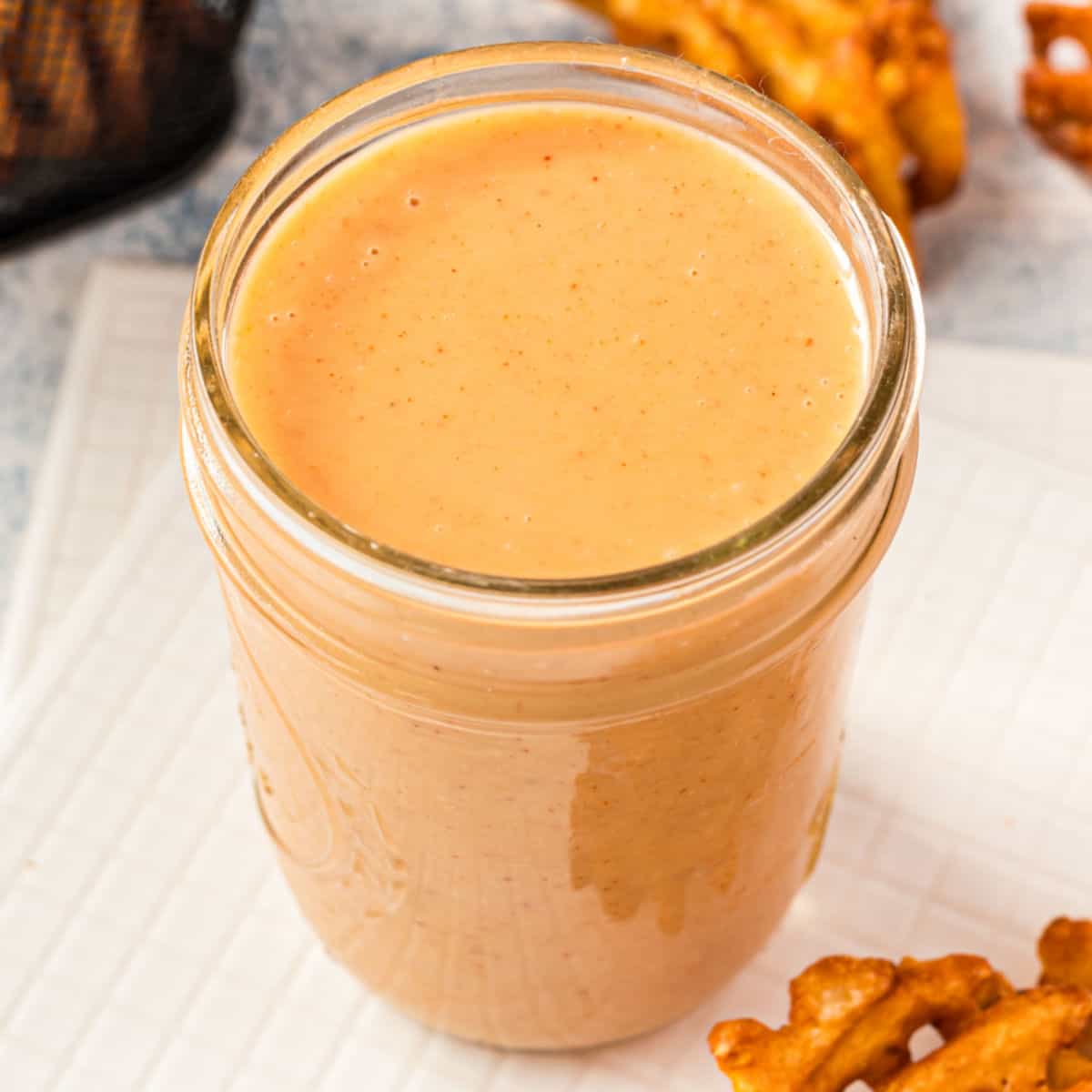 square image of copycat chick fil a sauce in a mason jar next to waffle fries