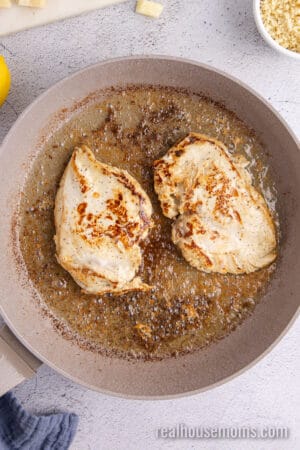 two marinated chicken breasts seared in a large skillet