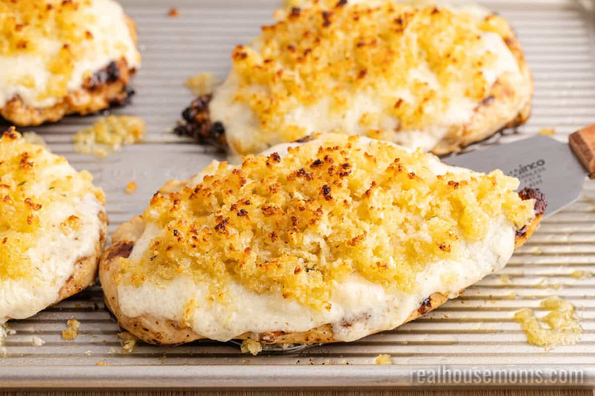 spatula under a Copycat Longhorn Parmesan Crusted Chicken breast on a baking sheet