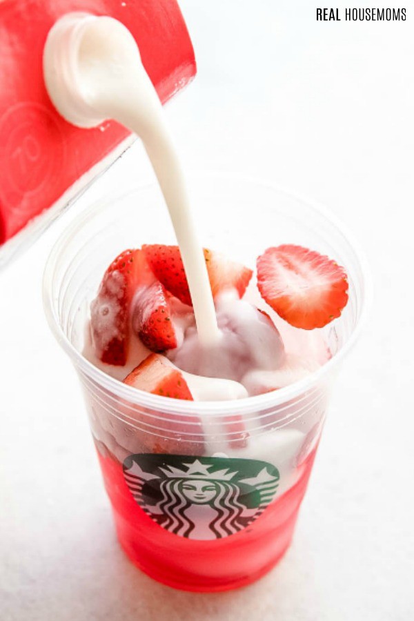 coconut milk being pour into cup with iced tea, instant refresher, ice and strawberries to make a copycat starbucks pink drink