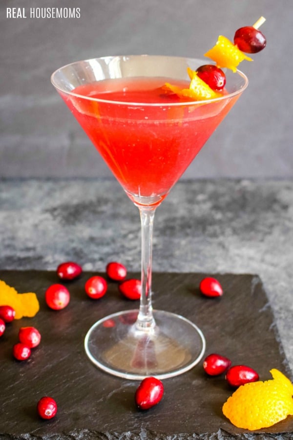 cosmopolitan cocktail in a martini glass garnished with cranberries and orange peel