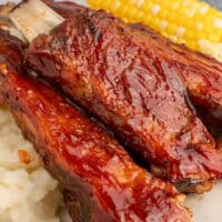 image of country style pork ribs on a plate with mashed potatoes and corn on the cob. The title of the post on top of the image in pink and black lettering