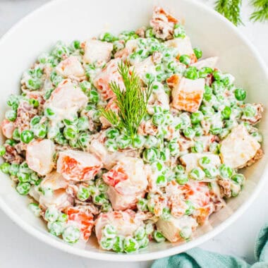 square image of crab, pea & bacon salad topped with fresh dill in a serving bowl