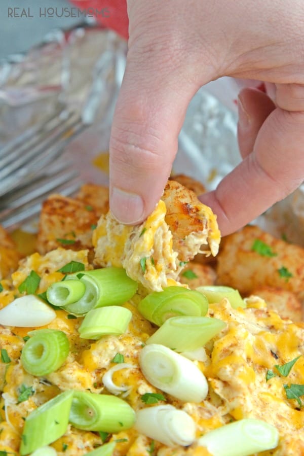 A hand reaching to take a bite-sized piece of Crabby Totchos