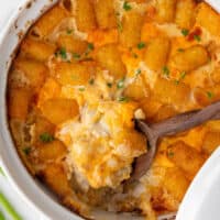 square image of crack chicken tater tot casserole in a baking dish with a wooden spoon