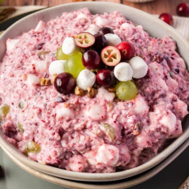 square image of cranberry fluff in a serving bowl with fruit, nuts an marshmallows on top