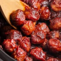 square image of a wooden spoon with cranberry meatballs on it