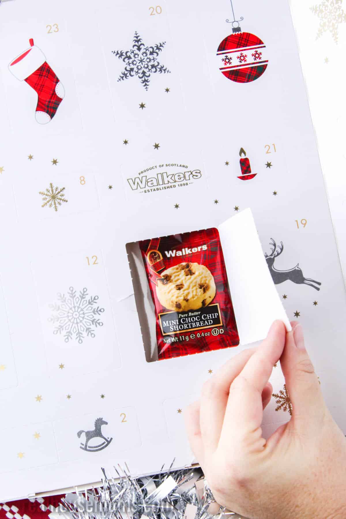 hand opening a Walk'ers shortbread advent calendar to reveal a mini choc chip shortbread inside one door