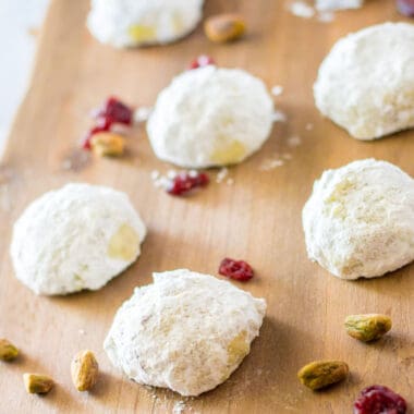 square image of russian tea cakes on a cutting board with pistachios and cranberries
