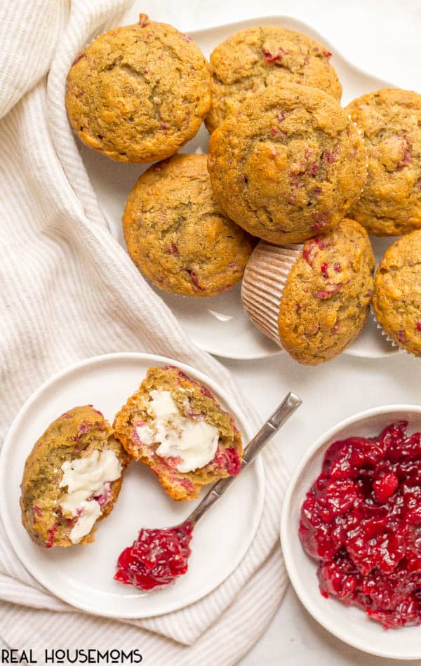 Cranberry Sauce Muffins piled on a plate, one muffin on a serving plate cut open and topped with butter